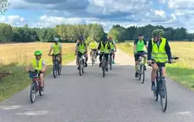 Grupa os&oacute;b w kamizelkach odblaskowych jedzie rowerami drogą asfaltową