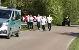 Grupa biegaczy na drodze asfaltowej pod eskortą Straży Granicznej