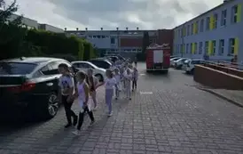 Dzieci z pierwszej klasy idą obok wozu strażackiego.
