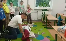 Grupa uczni&oacute;w przygląda się instruktorowi podczas zajęć pierwszej pomocy