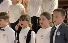 Uczniowie w strojach galowych śpiewa piosenkę