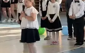 Uczennica trzyma w ręku mikrofon i przemawia do zgromadzonych gości