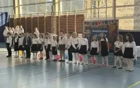 Grupa uczni&oacute;w z klasy pierwszej stoi w rzędzie i śpiewa piosenkę