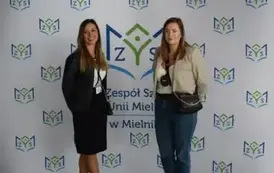 Absolwenci z uśmiehem pozują na tle ścianki