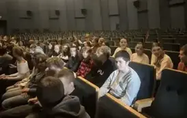 Uczniowie siedzą na krzesełkach i oczekują na rozpoczęcie spektaklu