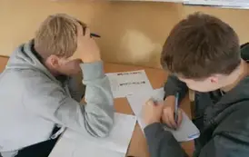 Chłopcy siedzą w ławce i wykonują zadanie
