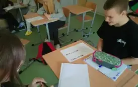 Uczniowie siedzą w ławce i wykonują zadanie
