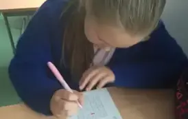 Dziewczynka siedzi w ławce i rozwiązuje zadanie