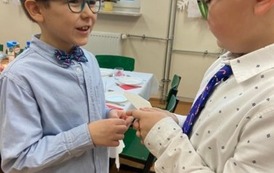 Dwaj chłopcy w eleganckich strojach dzielą się opłatkiem i składają sobie życzenia