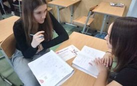 Uczennice siedzą w ławce i wykonują karty pracy