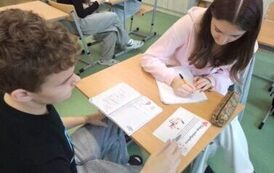 Uczniowie siedzą w ławce i wykonują zadania