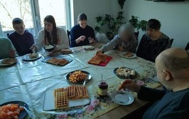 Osoby siedzą przy stole jedząc gofry