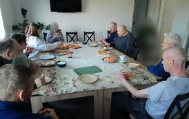 Osoby siedzą przy stole, jedzą gofry