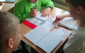 Uczniowie  siedzą przy stoliku i rozwiązują zadanie.