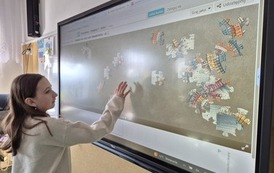 Dziewczynka układa puzzle na tablicy multimedialnej