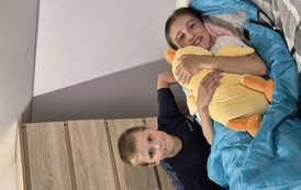 Dziewczynka leży z ż&oacute;łtym pluszakiem, za nią kuca chłopiec w ciemnym stroju