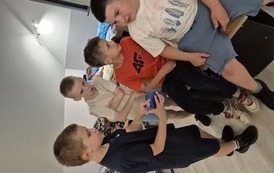 Czterech chlopc&oacute;w w pokoju, jeden z nich pokazuje coś na telefonie