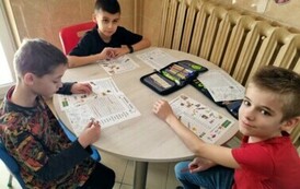 Trzech chłopc&oacute;w siedzi przy stole, rozwiązują zadania.