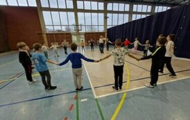 Uczniowie na hali sportowej stoją w kręgu trzymając się za ręce