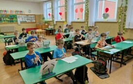 Dziewczynki i chłopcy siedzą w ławkach szkolnych, grają na fletach
