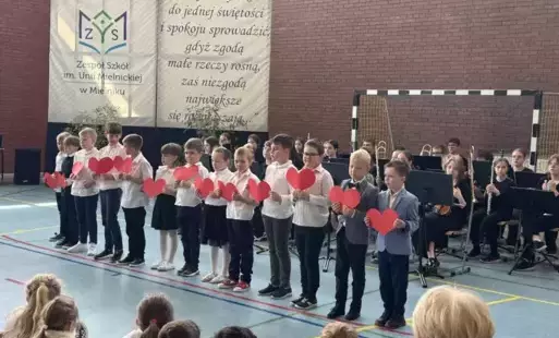 Uczniowie trzymają papierowe serca i śpiewają piosenkę 