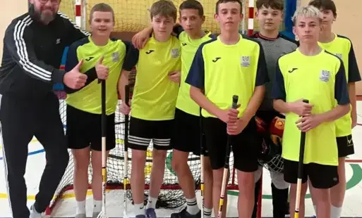 Uczniowie ubrani w stroje sportowe pozują z trenerem do zdjęcia
